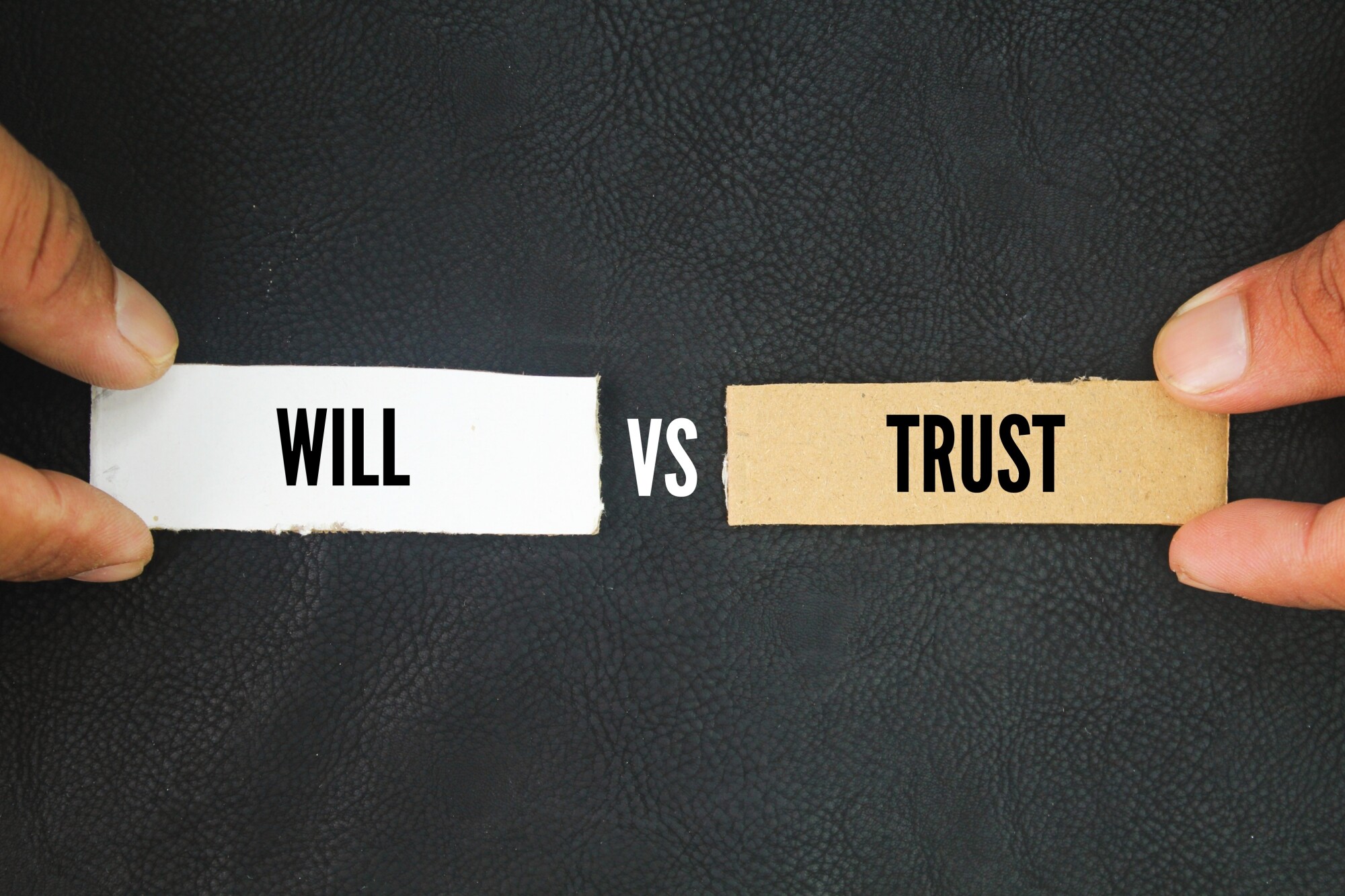 Hands hold white and brown strips of paper, one strip says "will" and one says "trust" with word "Vs" in between strips